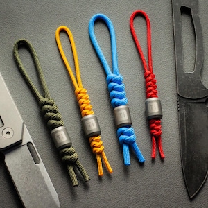 May include: Five colorful paracord keychains with a titanium bead. Each keychain has a different color: green, yellow, blue, red, and black.