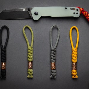 May include: Five different colored paracord keychains with copper beads. The keychains are black, green, gray, yellow, and red. The keychains are all made with the same knot pattern.