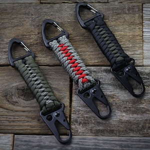 May include: Three keychains with black metal clips and braided paracord straps. The straps are in different color combinations of black, green, and red.