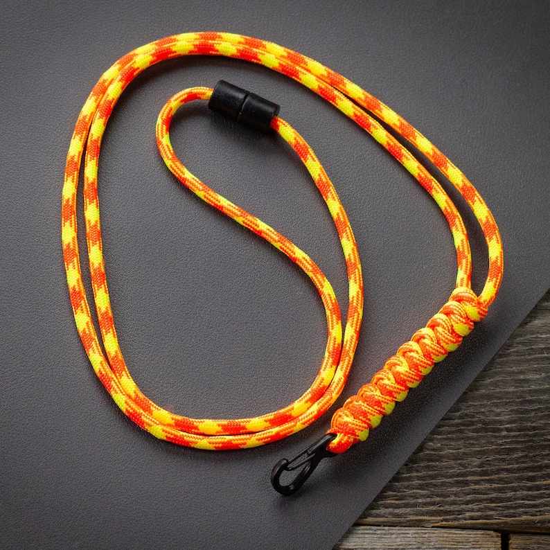 May include: A lanyard with a yellow and orange pattern. The lanyard has a black clasp and a black magnetic clasp. The lanyard is made of a woven rope material.