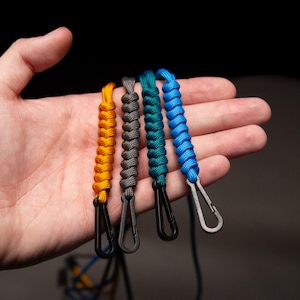 Hand holding four Paracord ID Lanyards in assorted colors, showing compact size and detailed craftsmanship of the non-ferrous MRI-safe badge holders.