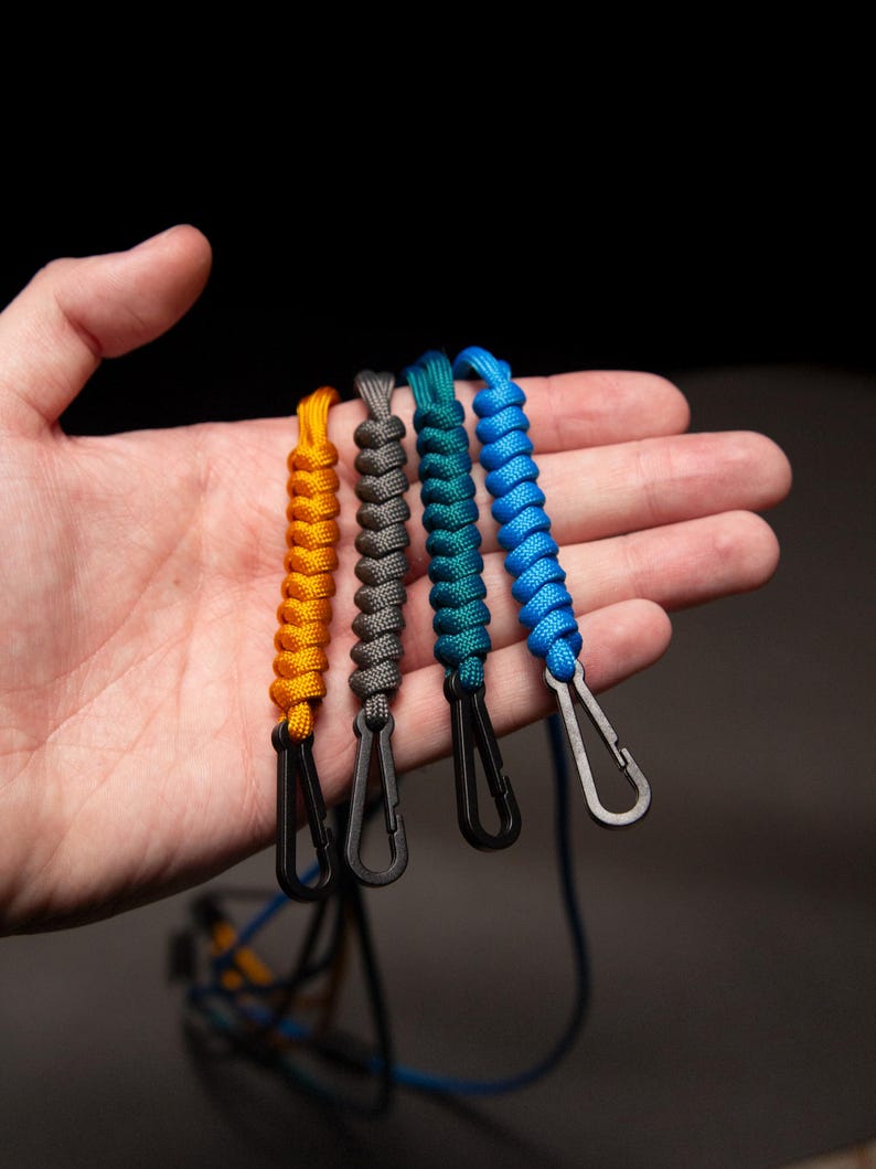 Hand holding four Paracord ID Lanyards in assorted colors, showing compact size and detailed craftsmanship of the non-ferrous MRI-safe badge holders.