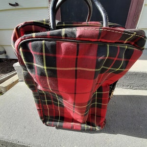 May include: Red, black, and yellow plaid travel bag with a black leather handle.
