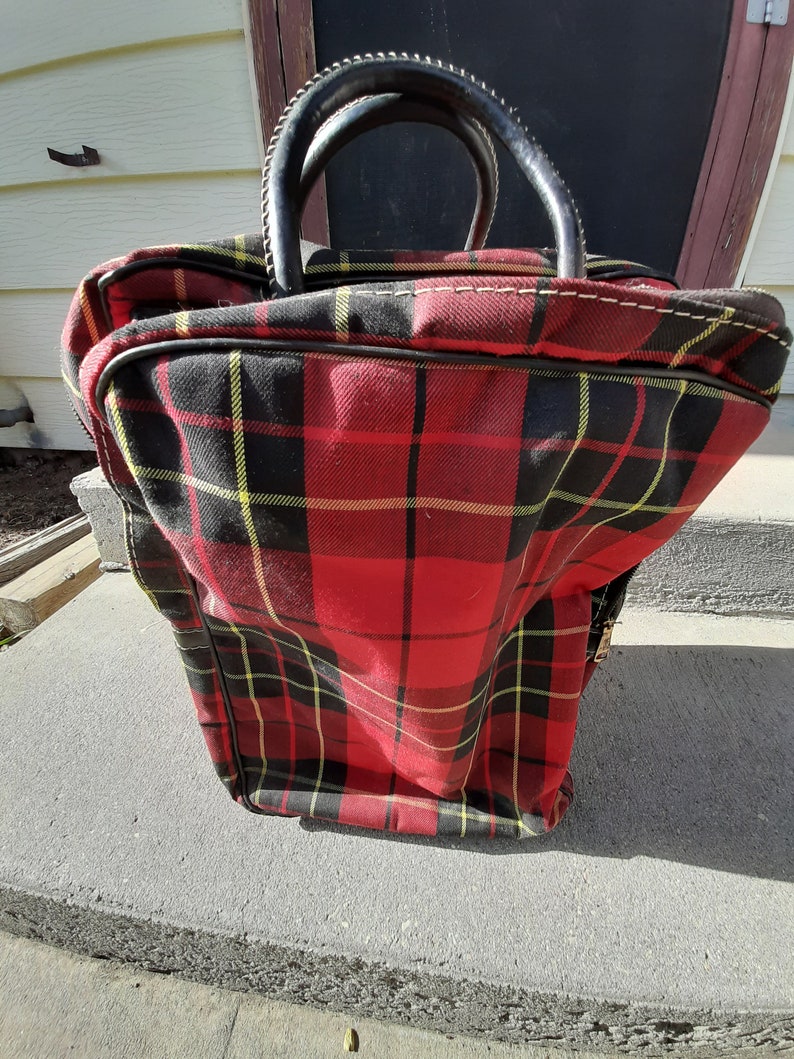 May include: Red, black, and yellow plaid travel bag with a black leather handle.