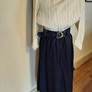 Puede incluir: Un vestido blanco de manga larga con falda azul marino y cinturón azul oscuro con hebilla dorada.