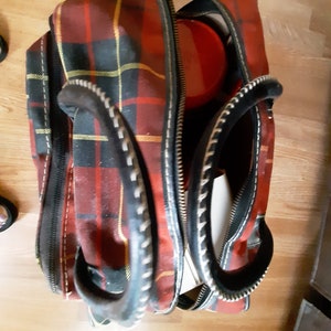 May include: A red, black, and yellow plaid travel bag with black leather handles and a zipper closure.