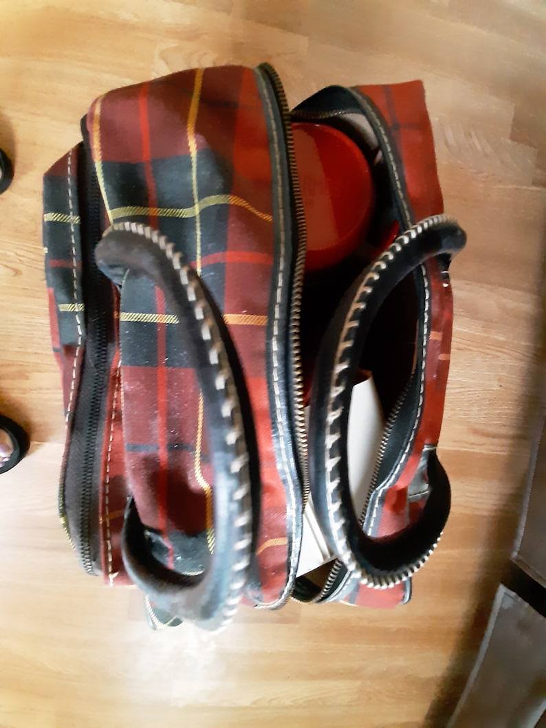 May include: A red, black, and yellow plaid travel bag with black leather handles and a zipper closure.