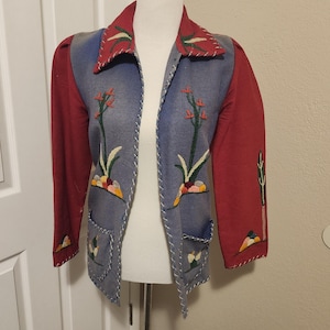 May include: A vintage jacket with a unique design. The jacket features a red collar and sleeves, with a blue denim-like front adorned with embroidered floral patterns. White stitching outlines the edges and pockets.