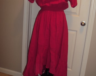 Könnte beinhalten: Ein knallrotes, knielanges Kleid mit kurzen Ärmeln und einer gerafften Taille. Das Kleid hat einen hohen Ausschnitt und einen leicht asymmetrischen Saum.