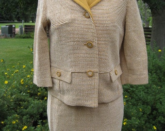 May include: A brown and white tweed suit with a yellow collar. The jacket has three buttons and a pocket on the front. The skirt is knee-length.
