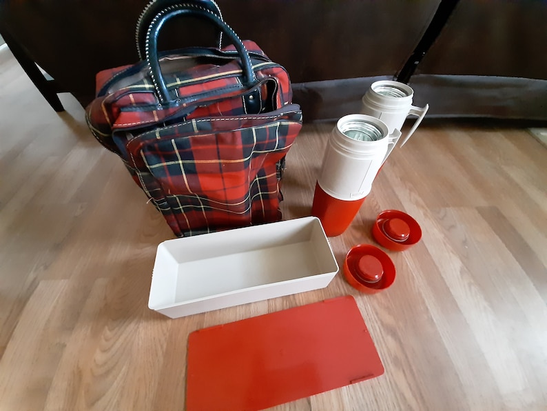 May include: A red and black plaid travel bag with two white and red thermoses, a white rectangular container, and two red lids.