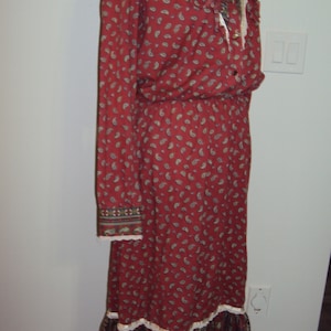 May include: A long-sleeved red dress with a paisley print and white lace trim. The dress has a gathered waist and a ruffled hem.