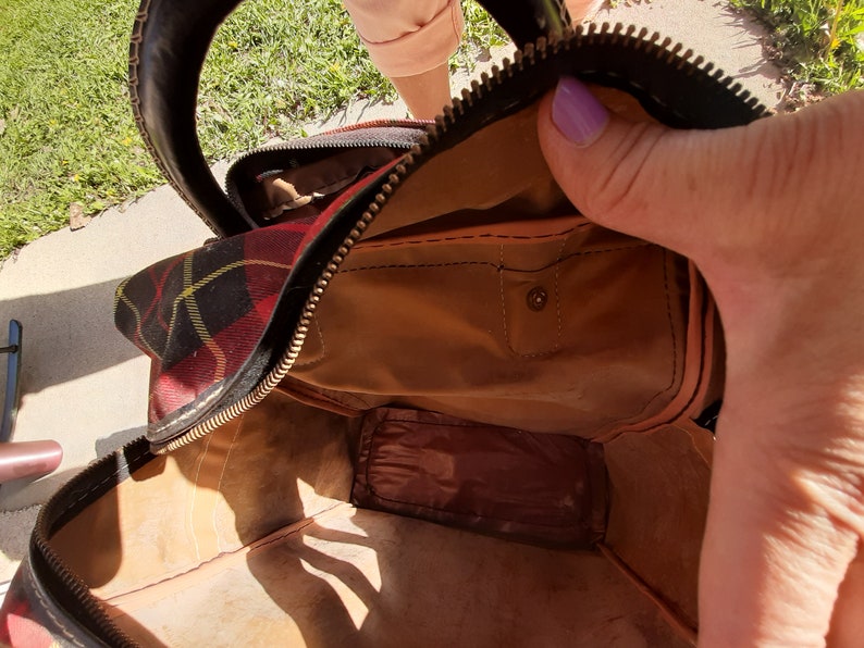 May include: A brown leather travel bag with a black zipper and a plaid lining. The bag is open and the inside is visible.