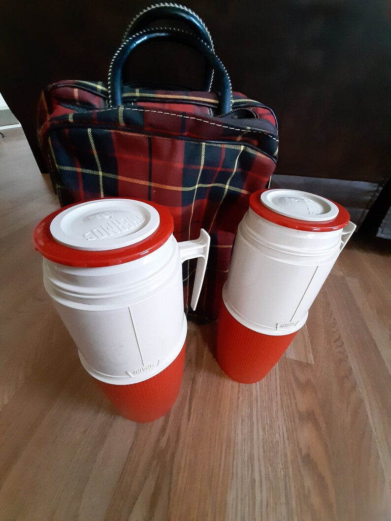 May include: Two red and white insulated thermos bottles with a red plaid travel bag. The thermos bottles have a white lid with a red band and a red base.