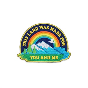 May include: An embroidered patch with a rainbow, mountains, and trees. The text reads "This land was made for you and me."