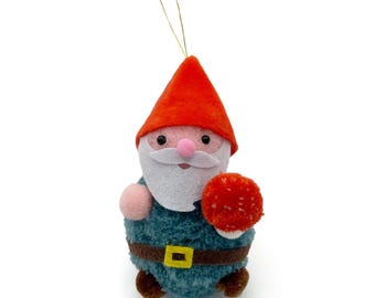 May include: A plush gnome ornament with a red pointed hat, white beard, and blue body. The gnome holds a red and white mushroom. A gold string is attached for hanging. The gnome has a brown belt with a yellow buckle.