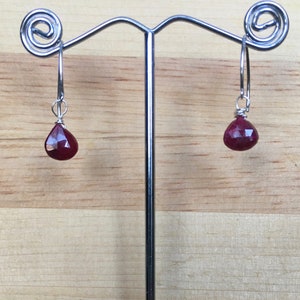 May include: A pair of silver hoop earrings with a teardrop-shaped red gemstone hanging from each hoop.