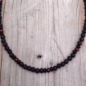Puede incluir: Un collar de cuentas de lava negra y piedras preciosas rojas con un cierre de plata.