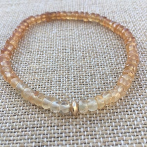 May include: A delicate bracelet made of small, faceted, light brown and clear beads with a gold bead accent.