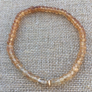 May include: A gold bracelet made of small, faceted, amber-colored beads. The bracelet has a gold bead clasp.
