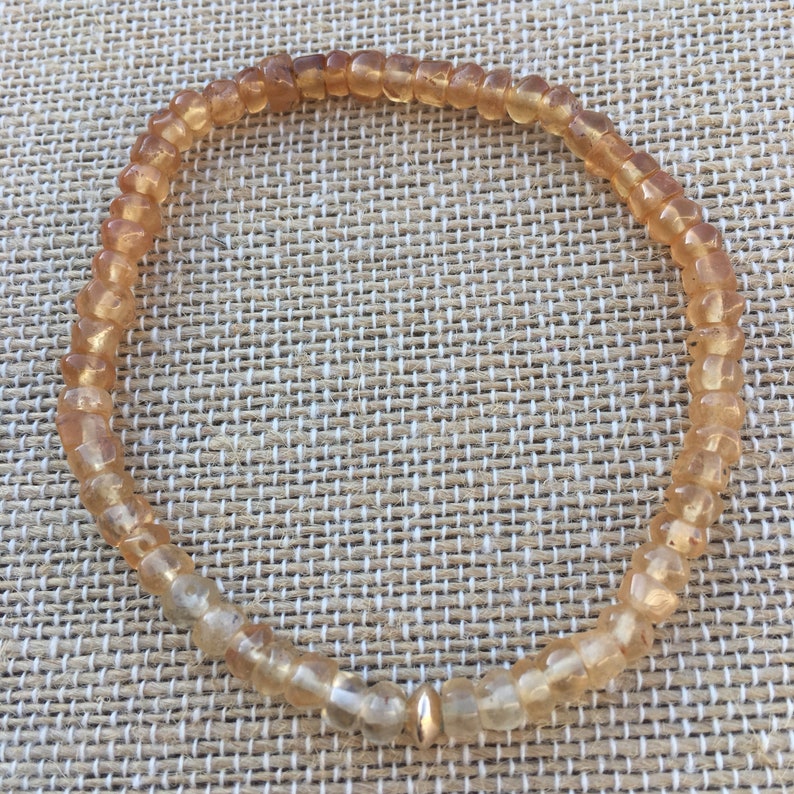 May include: A gold bracelet made of small, faceted, amber-colored beads. The bracelet has a gold bead clasp.