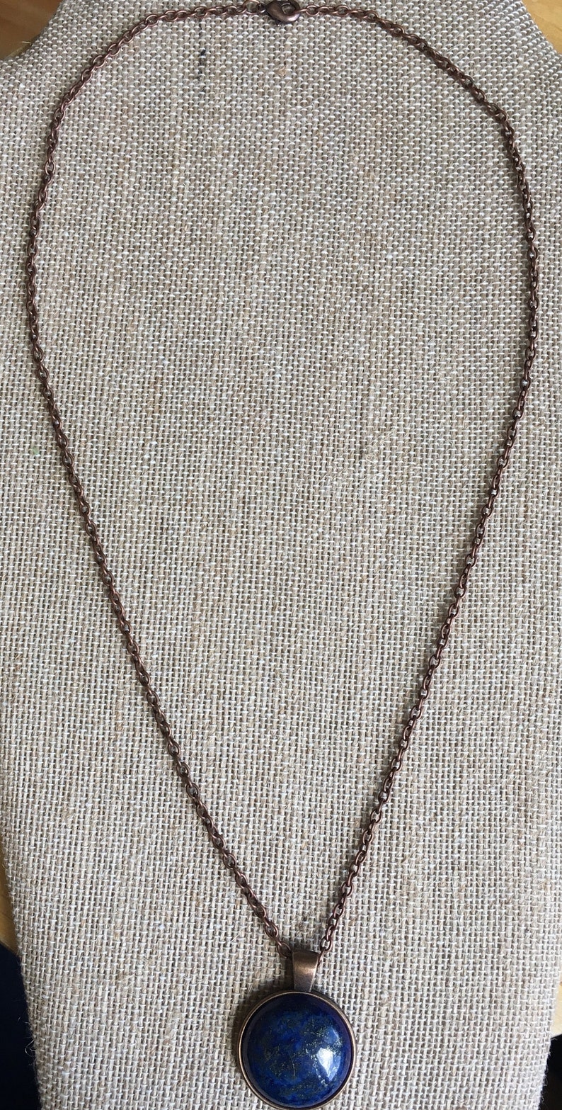 Puede incluir: Un collar de cadena de cobre con un colgante redondo con una piedra de lapisl&aacute;zuli azul.