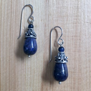 May include: A pair of silver dangle earrings with blue lapis lazuli stone drops and silver filigree accents.
