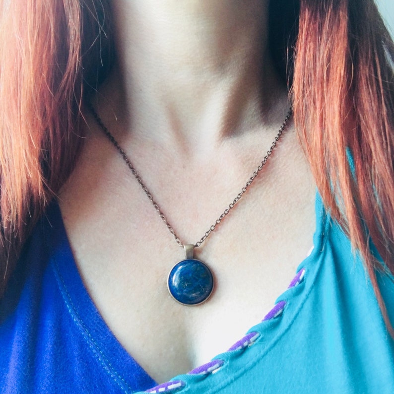 Puede incluir: Un collar de cadena de plata con un colgante redondo de lapisl&aacute;zuli azul. El colgante est&aacute; engastado en un bisel de plata.