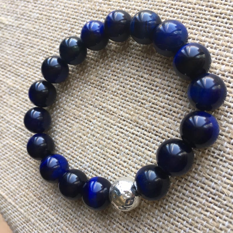 May include: A beaded bracelet featuring dark blue and black spherical beads with a silver accent bead. The bracelet is made of polished, round beads, showcasing a mix of deep blue and black hues. The silver bead adds a contrasting metallic element.