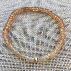 May include: A delicate bracelet made of small, light brown and clear beads with a gold bead accent.