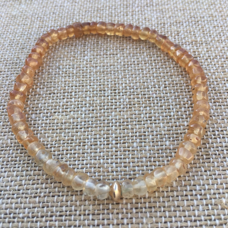 May include: A delicate bracelet made of small, light brown and clear beads with a gold bead accent.