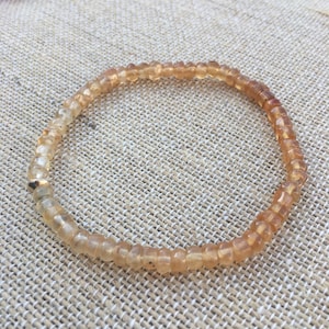 May include: A delicate bracelet made of small, light brown beads. The bracelet is strung on a thin gold chain.