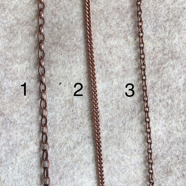 Puede incluir: Tres estilos diferentes de cadena de cobre, etiquetados como 1, 2 y 3. Las cadenas se muestran sobre un fondo marr&oacute;n claro.