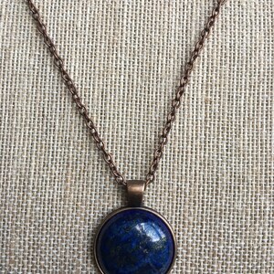Puede incluir: Un collar de cadena de cobre con un colgante redondo con una piedra de lapisl&aacute;zuli azul.