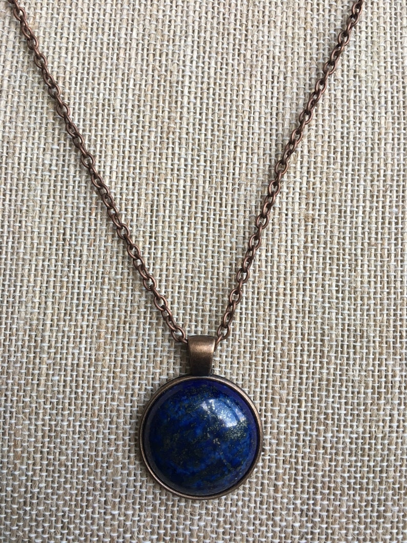 Puede incluir: Un collar de cadena de cobre con un colgante redondo con una piedra de lapisl&aacute;zuli azul.