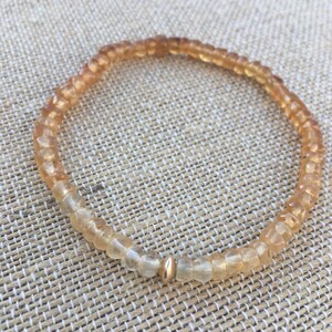 May include: A delicate bracelet made of small, faceted, light brown and clear beads with a gold accent bead.