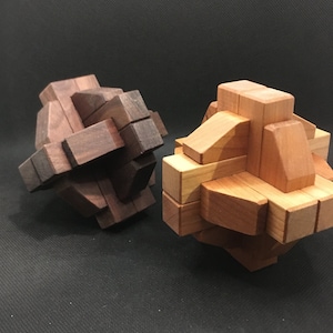 May include: Two wooden puzzles, one is dark brown and the other is light brown. Both puzzles are in the shape of a sphere and are made of interlocking pieces.