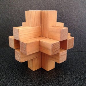 May include: A wooden puzzle made of multiple interlocking pieces, forming a star shape. The puzzle is made of light brown wood and has a natural finish.