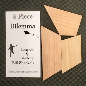 May include: A wooden puzzle with three pieces, designed and made by Bill Sheckels. The puzzle is called "3 Piece Dilemma" and features a silhouette of a person flying a kite. The puzzle is made of light brown wood with a natural grain pattern. The text "BlackDogPuzzleWorks.com" is printed on the card.