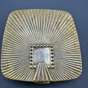 May include: A gold-toned metal compact with a sunburst design and a square, beveled mirror. The mirror is surrounded by a border of small, raised pyramids.