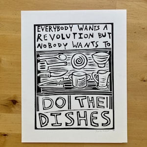 May include: Black and white linocut print with the text "Everybody wants a revolution but nobody wants to do the dishes". The print features a stylized illustration of a kitchen sink with dishes and utensils.