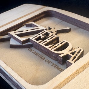 May include: A wooden sign with the words "Zelda Ocarina of Time" carved into it. The letters are layered and have a 3D effect.