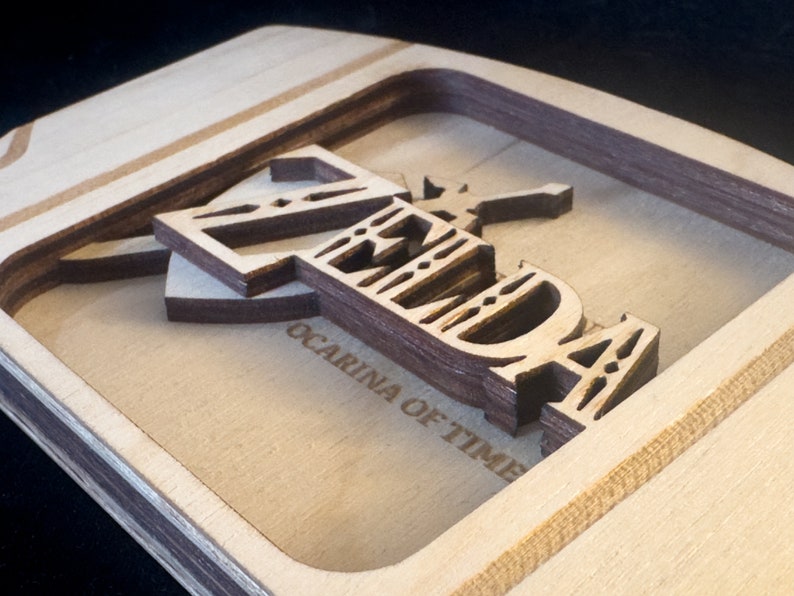 May include: A wooden sign with the words "Zelda Ocarina of Time" carved into it. The letters are layered and have a 3D effect.