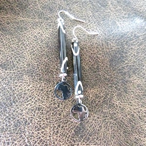 May include: A pair of black drop earrings with silver-coloured accents. The earrings have a cylindrical black body with white accents and a circular charm depicting the African continent.