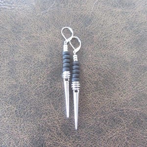 May include: A pair of silver-tone earrings with a black bead and spike design. The earrings have a lever back closure and are displayed against a brown background. The earrings are a unique accessory.