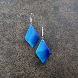 May include: A pair of blue and silver diamond-shaped earrings. The earrings have a gradient of blue colors, from a light blue to a dark blue.