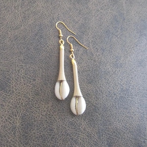 May include: A pair of gold-coloured earrings with white shell pendants. The earrings have a long, slender design with a coiled wire detail and a hook closure. The shells have a natural, organic shape.