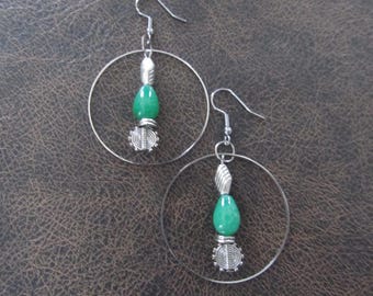 May include: A pair of silver-toned hoop earrings featuring a central vertical drop component. Each earring consists of a smooth silver hoop, a small silver-toned bead, a teardrop-shaped green bead, and a circular silver-toned textured charm.