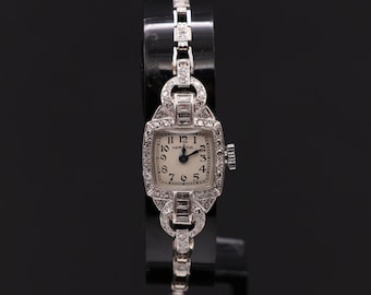 Könnte beinhalten: Eine Vintage-Hamilton-Armbanduhr mit quadratischem Zifferblatt und diamantbesetzter Lünette. Die Uhr hat ein weißes Zifferblatt mit schwarzen römischen Ziffern als Stundenmarkierungen und schwarzen Zeigern. Die Uhr ist auf einem schwarzen Hintergrund platziert.