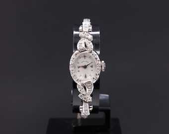 May include: A silver wristwatch with a white face and diamond accents on the band and bezel.